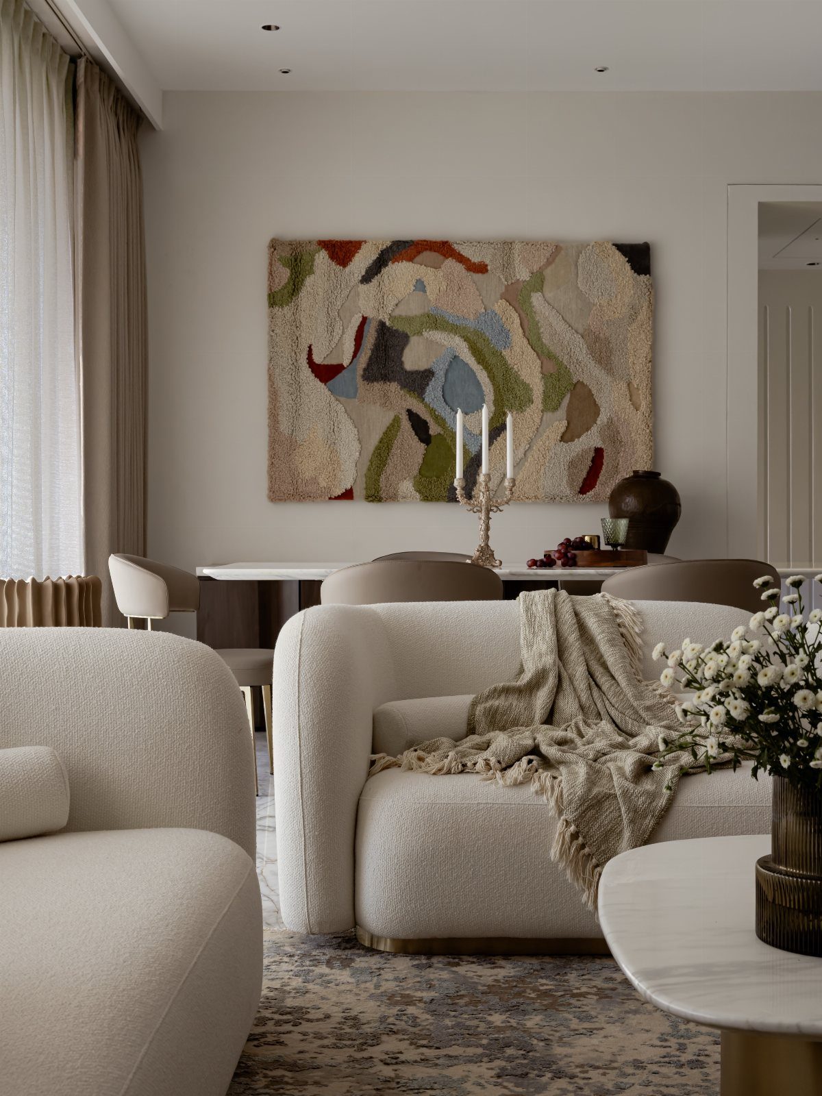 Cream bouclé armchairs with a textured throw blanket and abstract woven wall art.