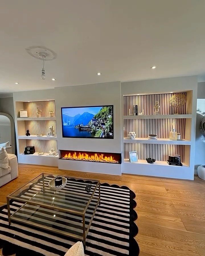 Built-in white recessed shelving flanking a wall-mounted TV and modern electric fireplace.