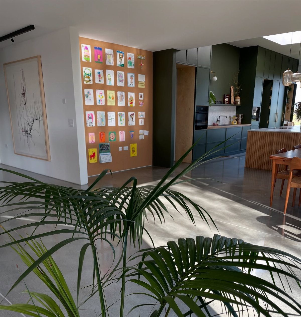 Cork accent wall covered in colorful children's drawings in a modern open living space.