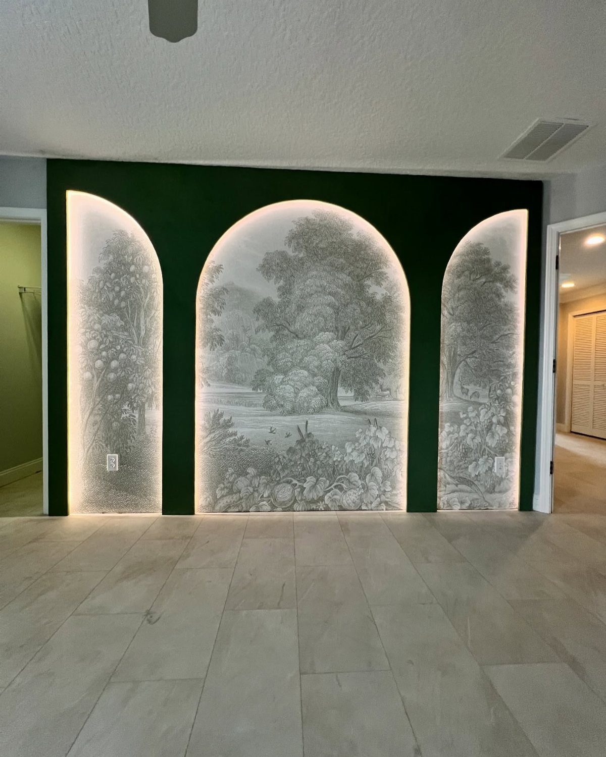 Dark green accent wall with three backlit arches featuring monochrome landscape wallpaper.