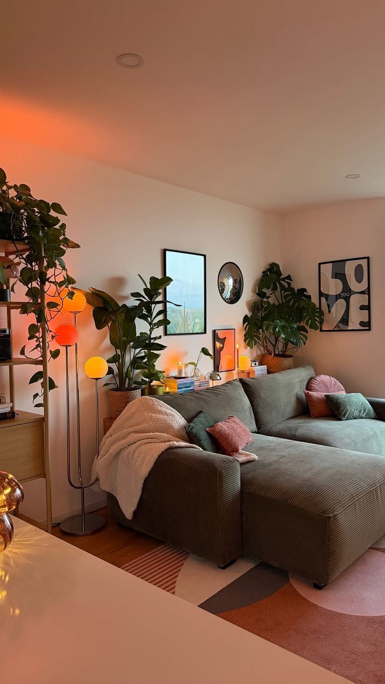 Green sectional sofa in a living room surrounded by lush green houseplants and warm lighting.