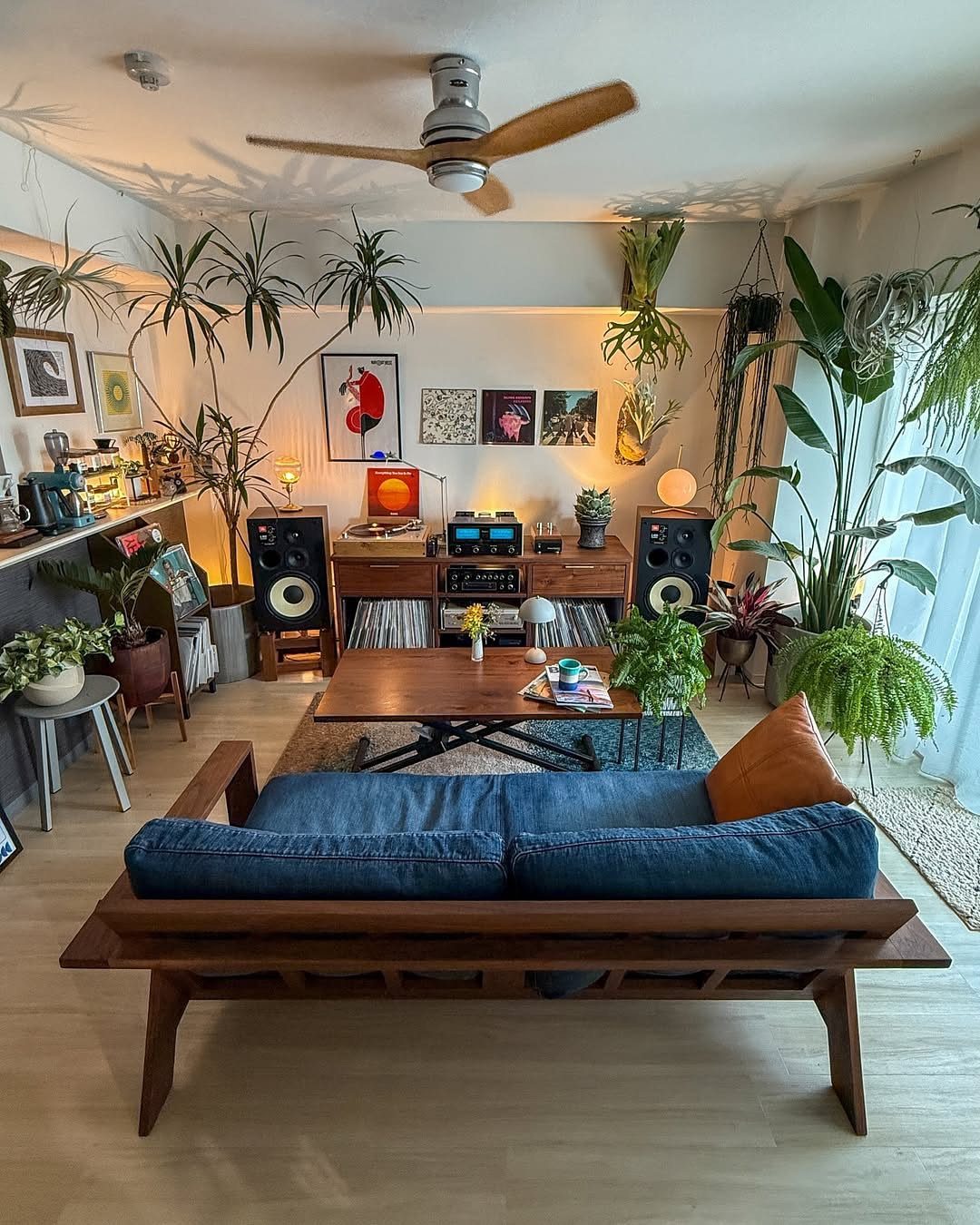 Living room with blue sofa, wooden furniture, diverse houseplants, and gallery wall art.