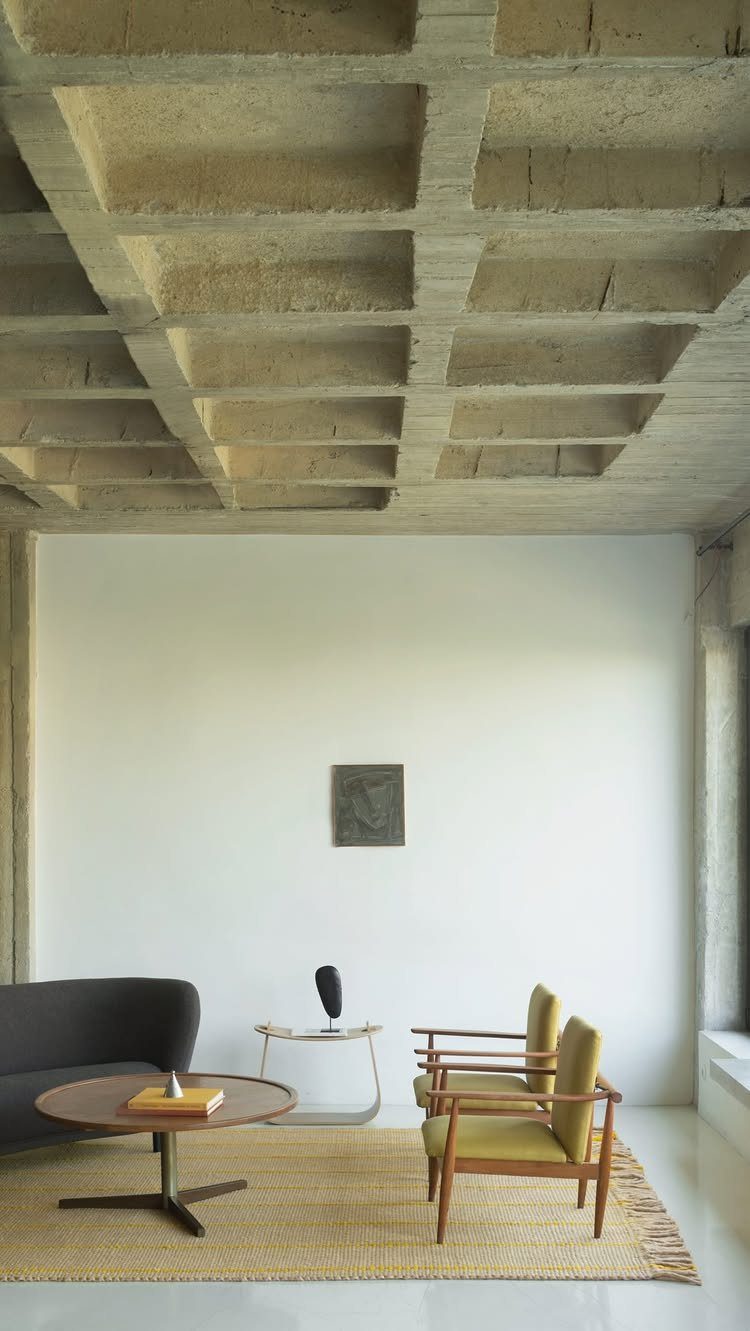Minimalist living room with yellow mid-century armchairs and a concrete waffle ceiling.