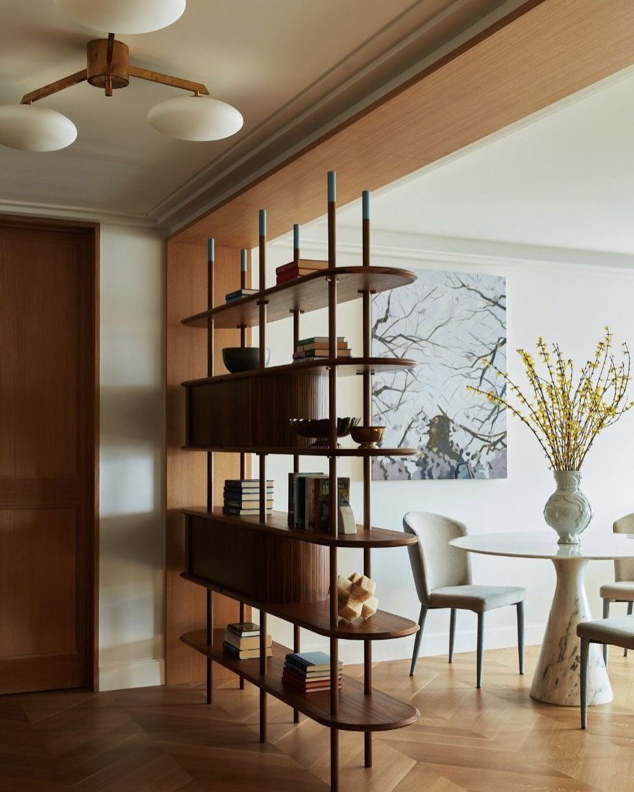 Open wooden bookcase divider separating a hallway from a modern dining room area.
