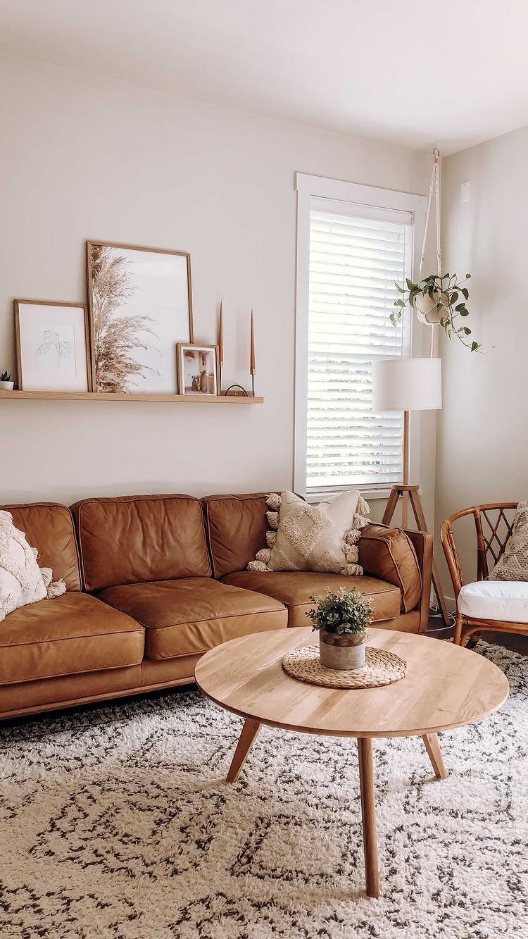 Brown leather couch with a wooden floating shelf holding framed art above it.
