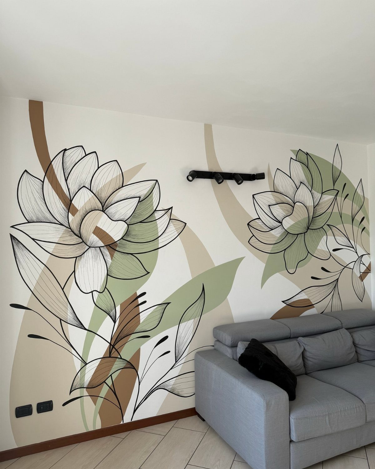 Grey couch positioned under a large floral wall mural in a living room.