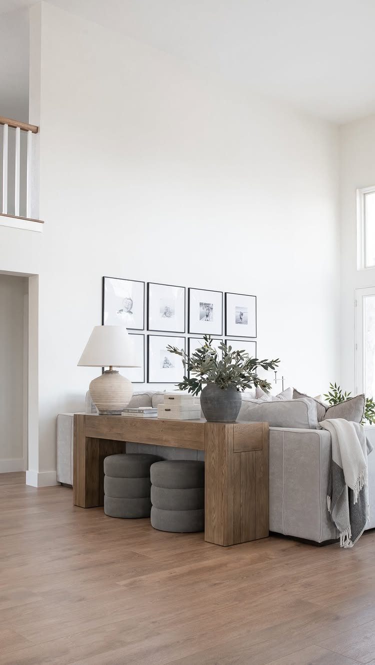 Wooden bar table positioned behind a grey sofa with two grey ottomans underneath.