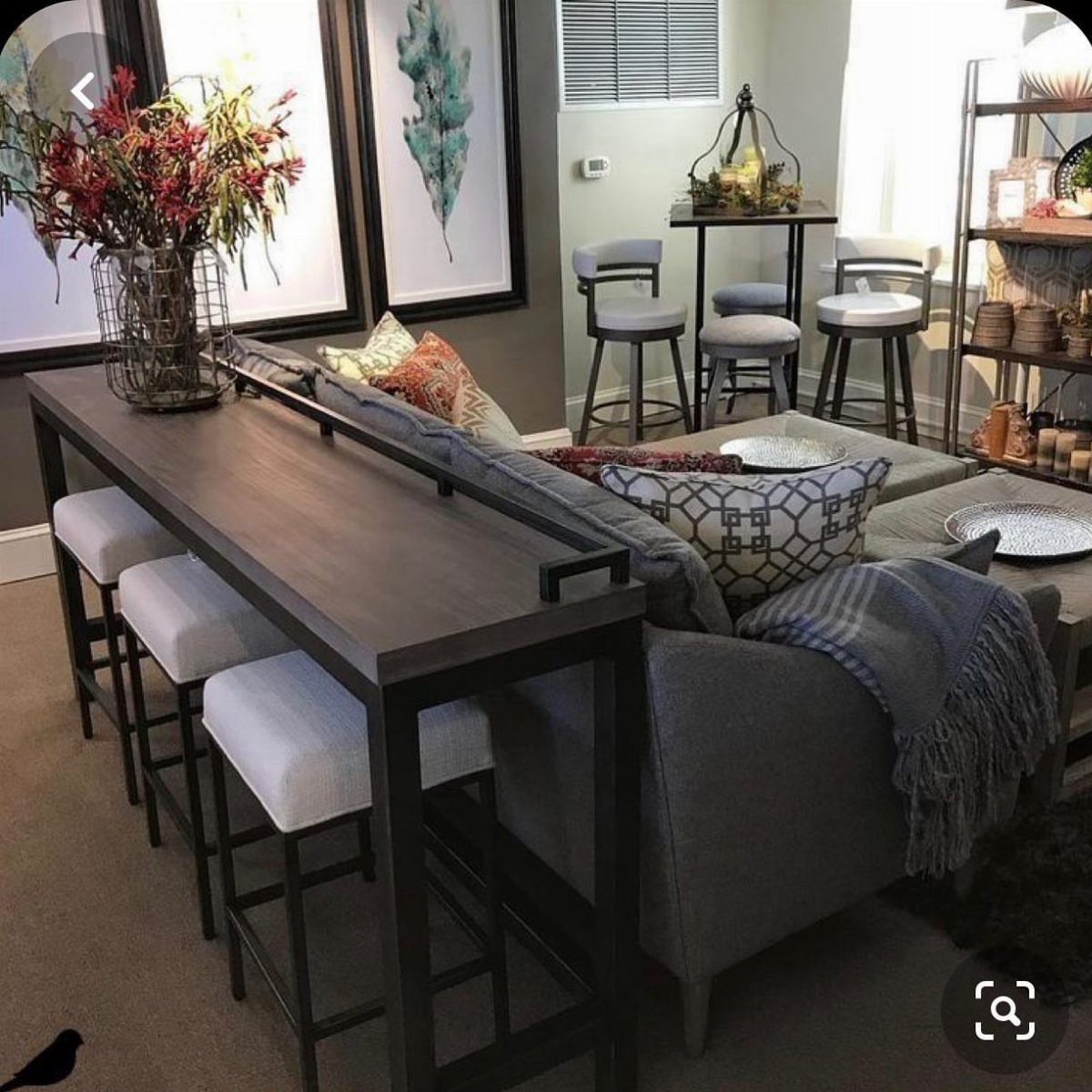 Dark wood bar table with white stools placed behind a grey sectional sofa.