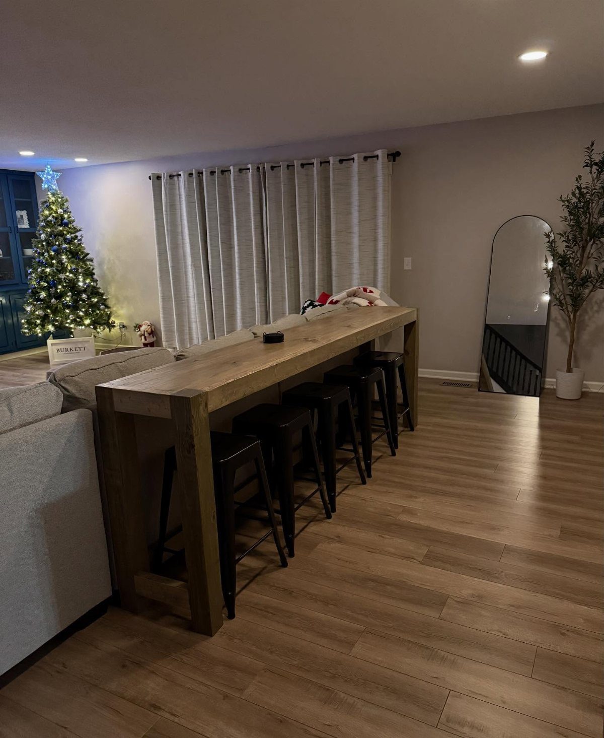 Long wooden bar table with black stools positioned behind a grey couch.