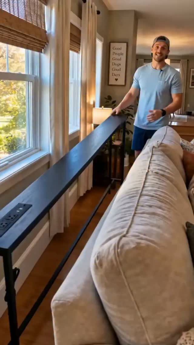 Long black bar table placed behind a beige couch in a bright living room.