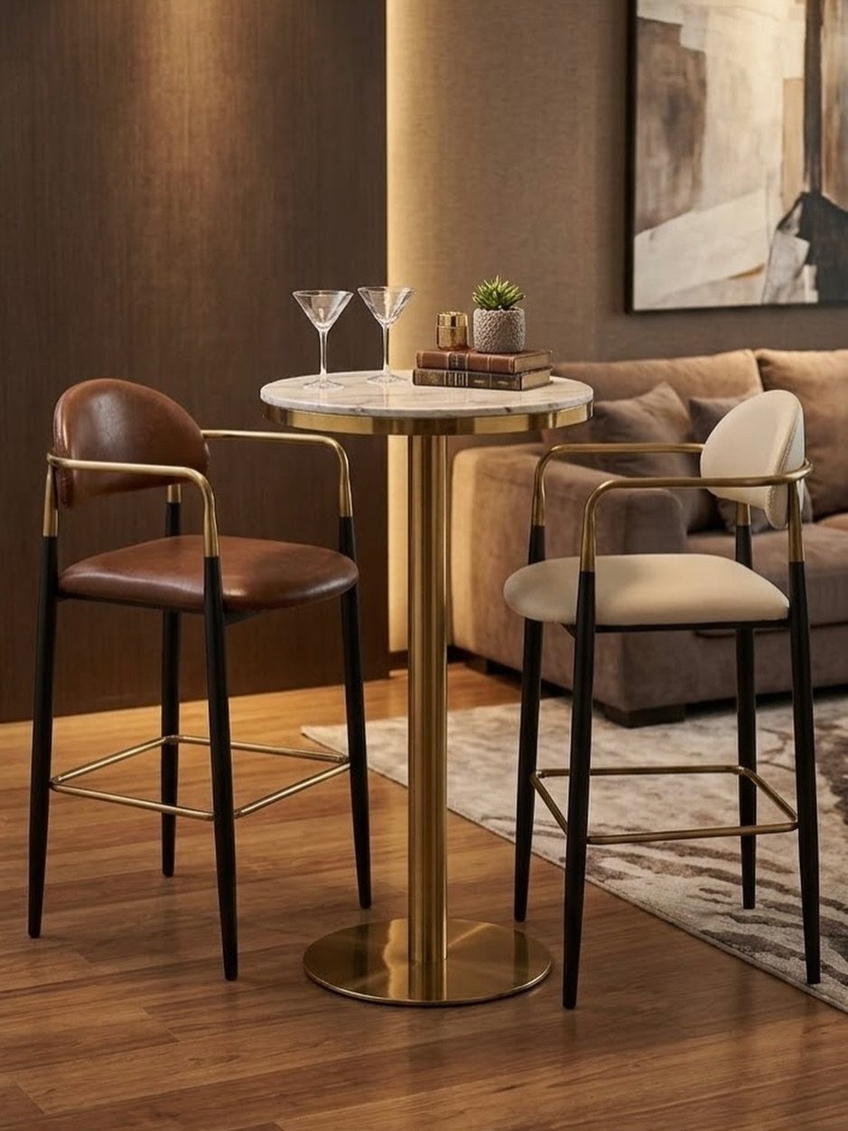Round marble bar table with gold base and two stools behind a tan sofa.