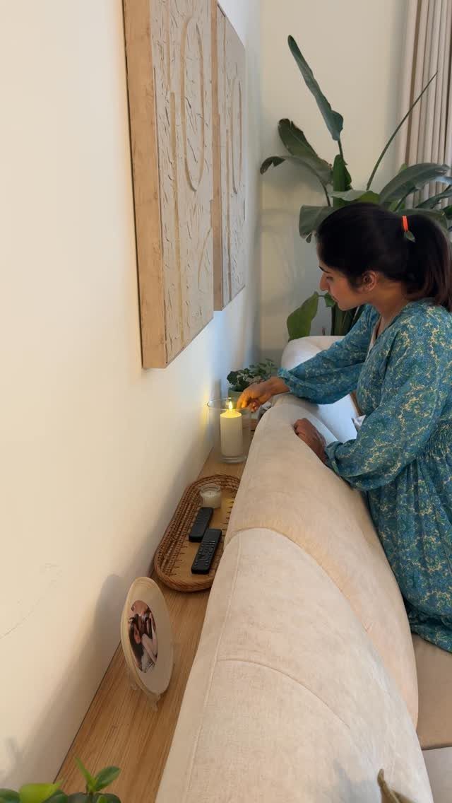 Woman standing behind a light sofa with carved wooden wall art and shelving.