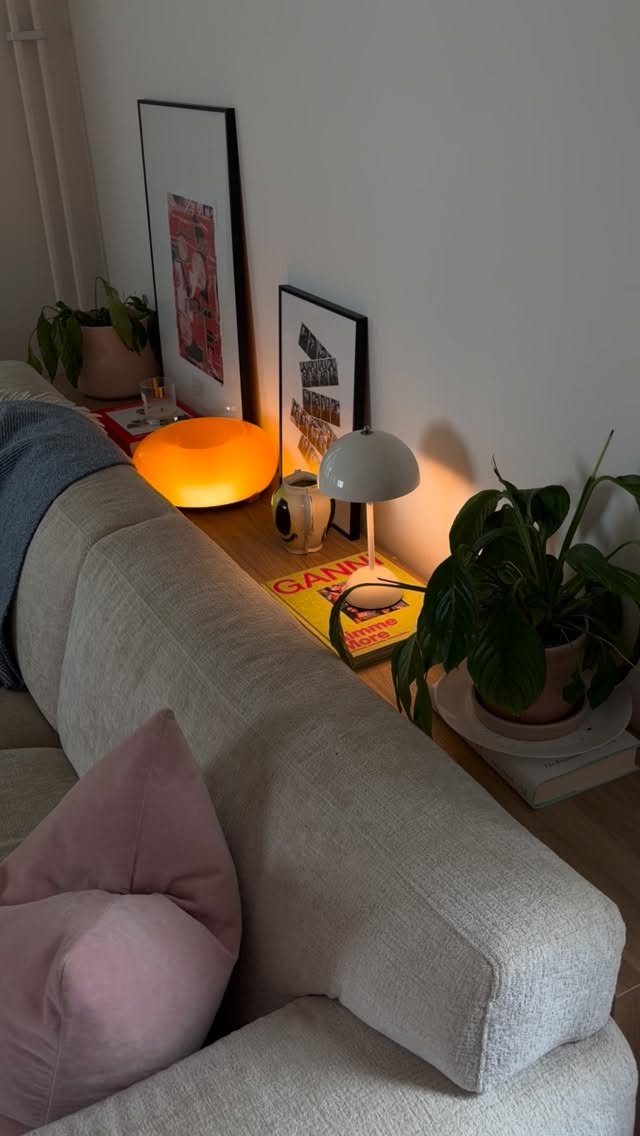 Grey sofa with a narrow shelf behind it holding lamps, plants, and art.