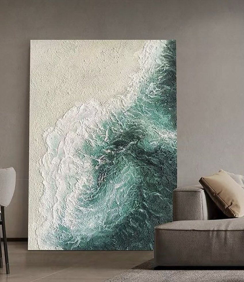 Large textured ocean wave painting leaning against a wall behind a grey sofa.