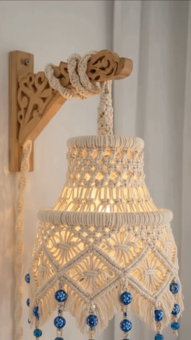 Macramé lampshade with blue beads hanging from a carved wooden wall bracket.