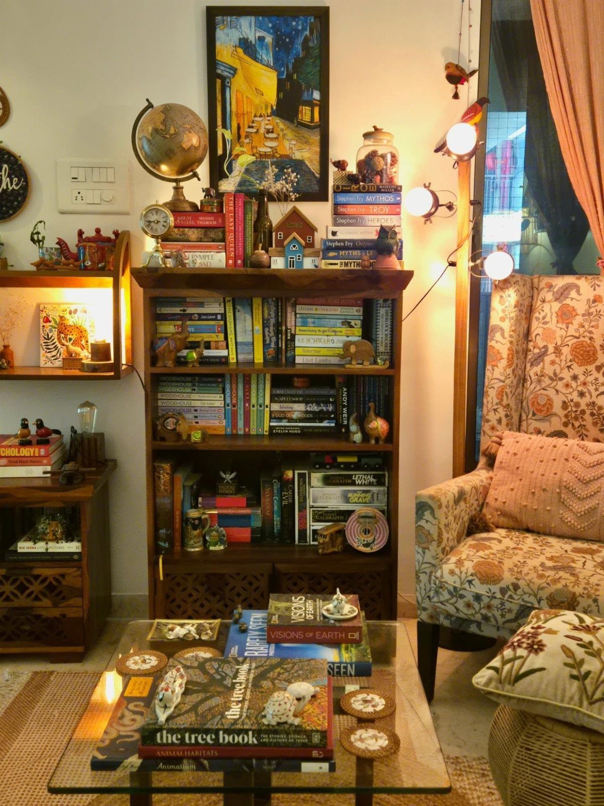 Patterned armchair with a pink cushion next to a tall wooden bookshelf.