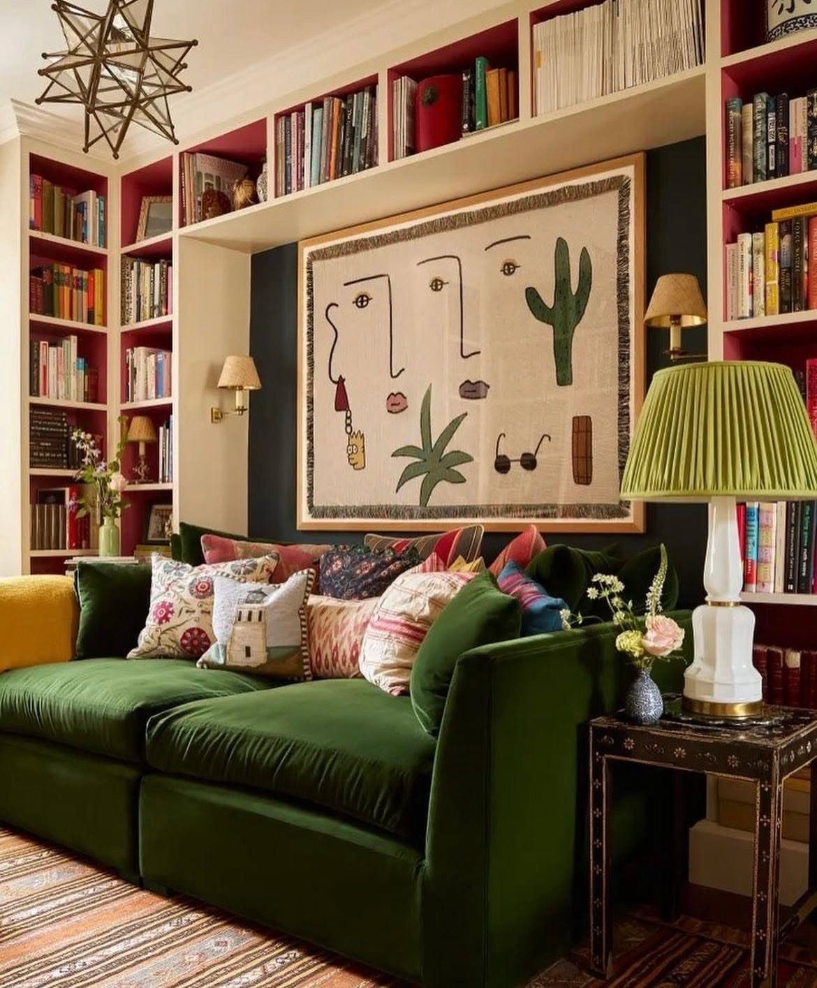 Green velvet sofa in a living room surrounded by bookshelves with red painted backs.