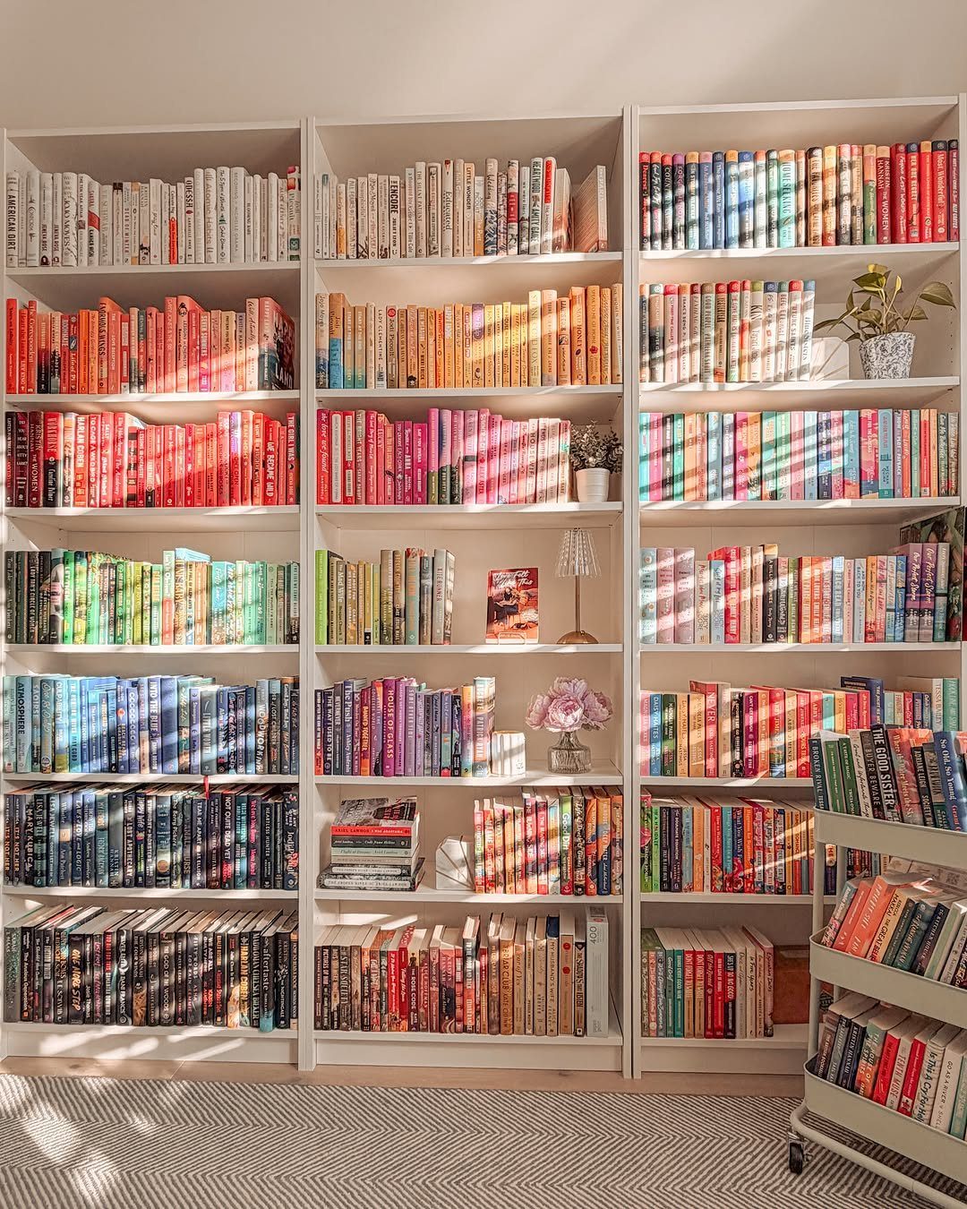White bookshelves filled with books organized in a rainbow color gradient pattern.