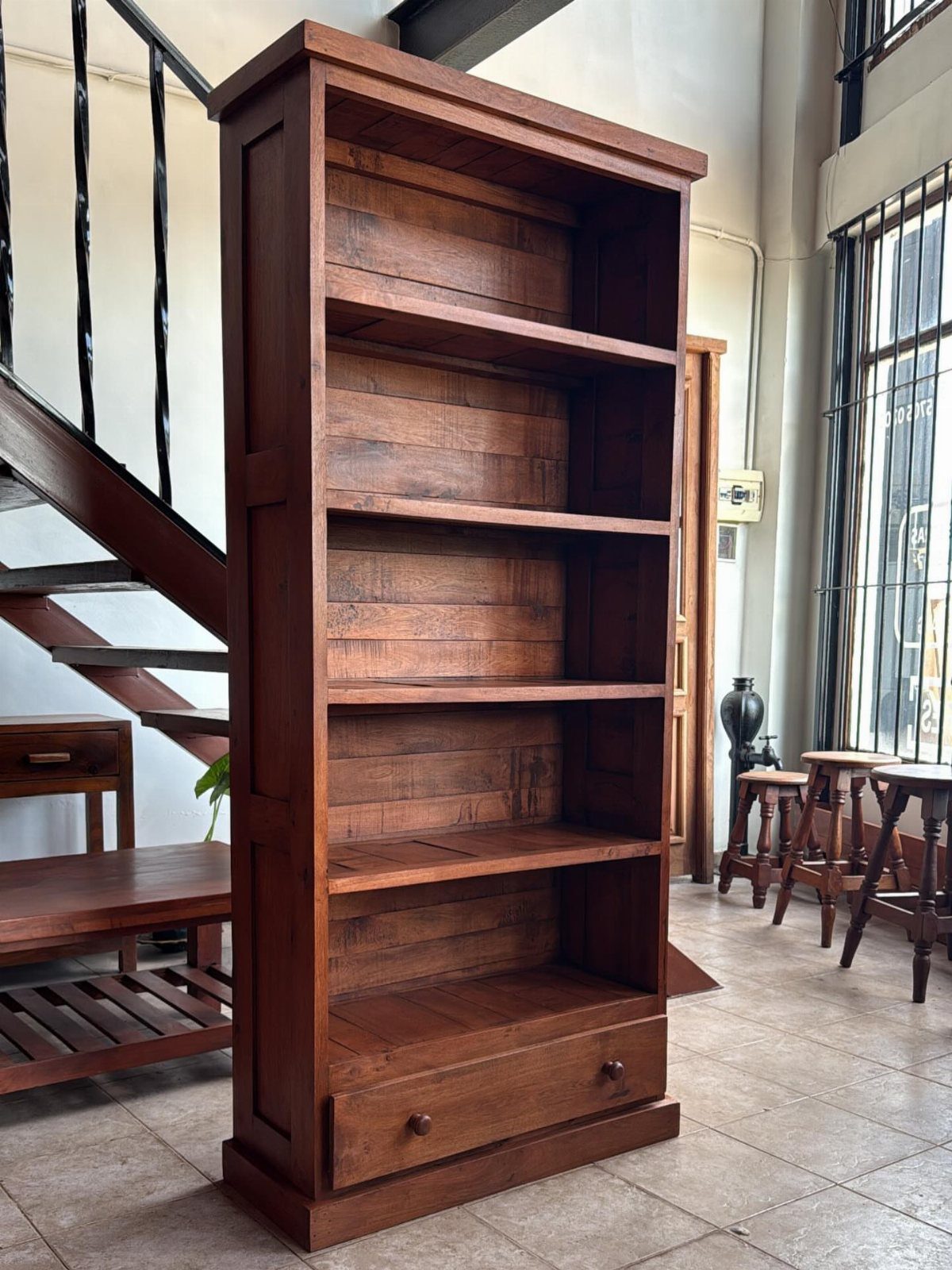 Tall brown reclaimed wood bookshelf with five shelves and a bottom drawer.