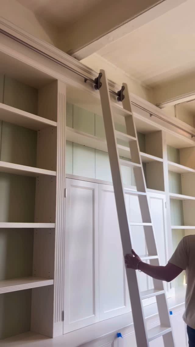 White rolling library ladder attached to a large built-in white bookshelf system.