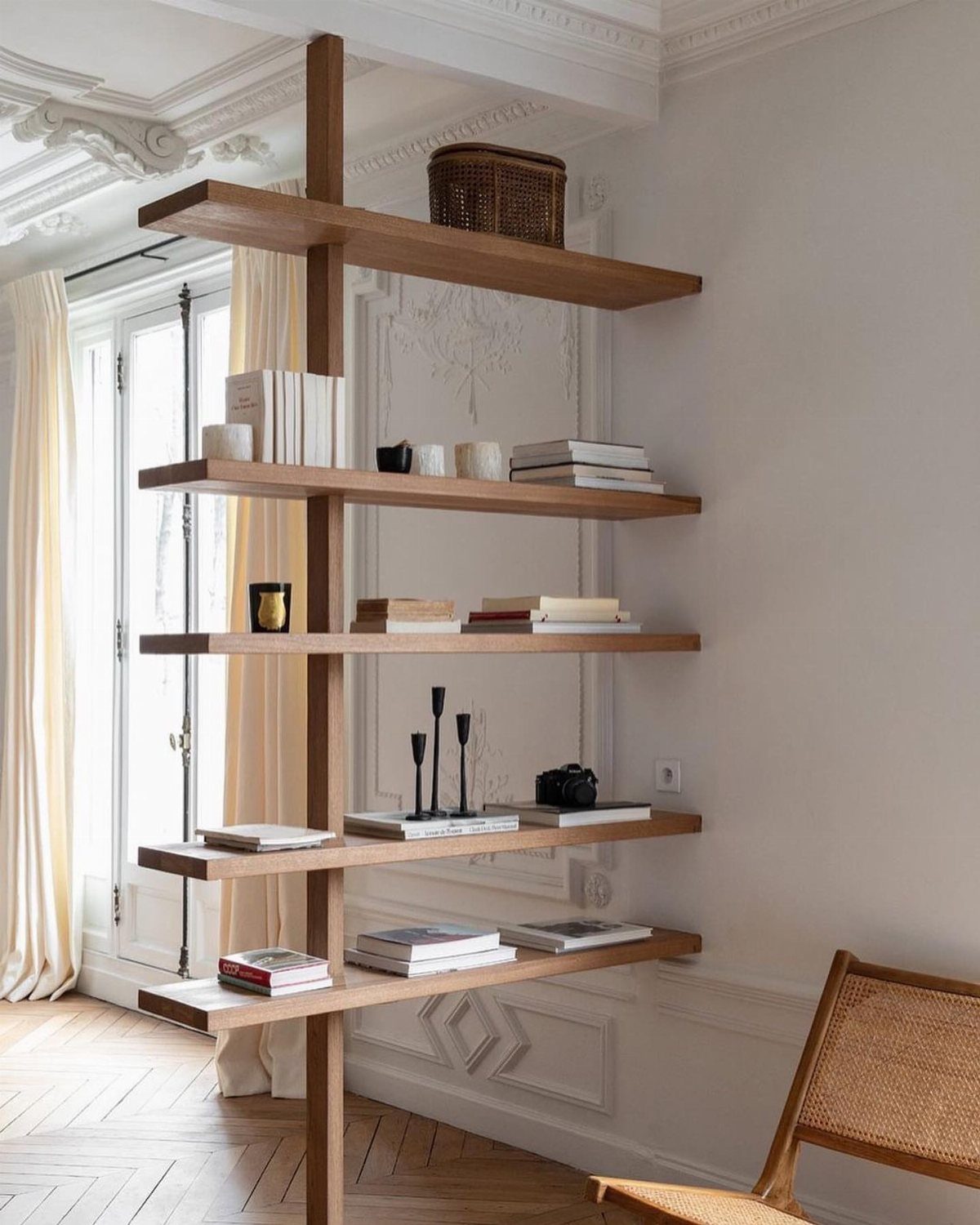 Wooden shelving unit holding books and decorative objects in a bright living room.