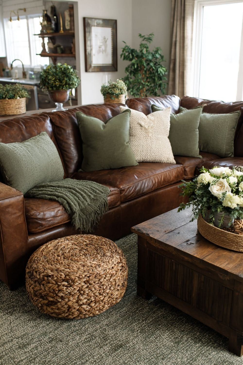 Brown leather sofa with green pillows and a green knitted throw blanket.