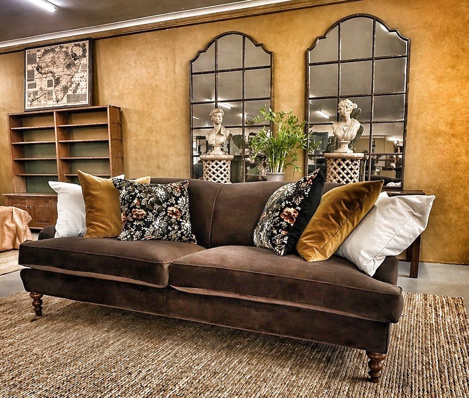 Dark brown velvet couch with mustard yellow and floral pillows in a rustic room.