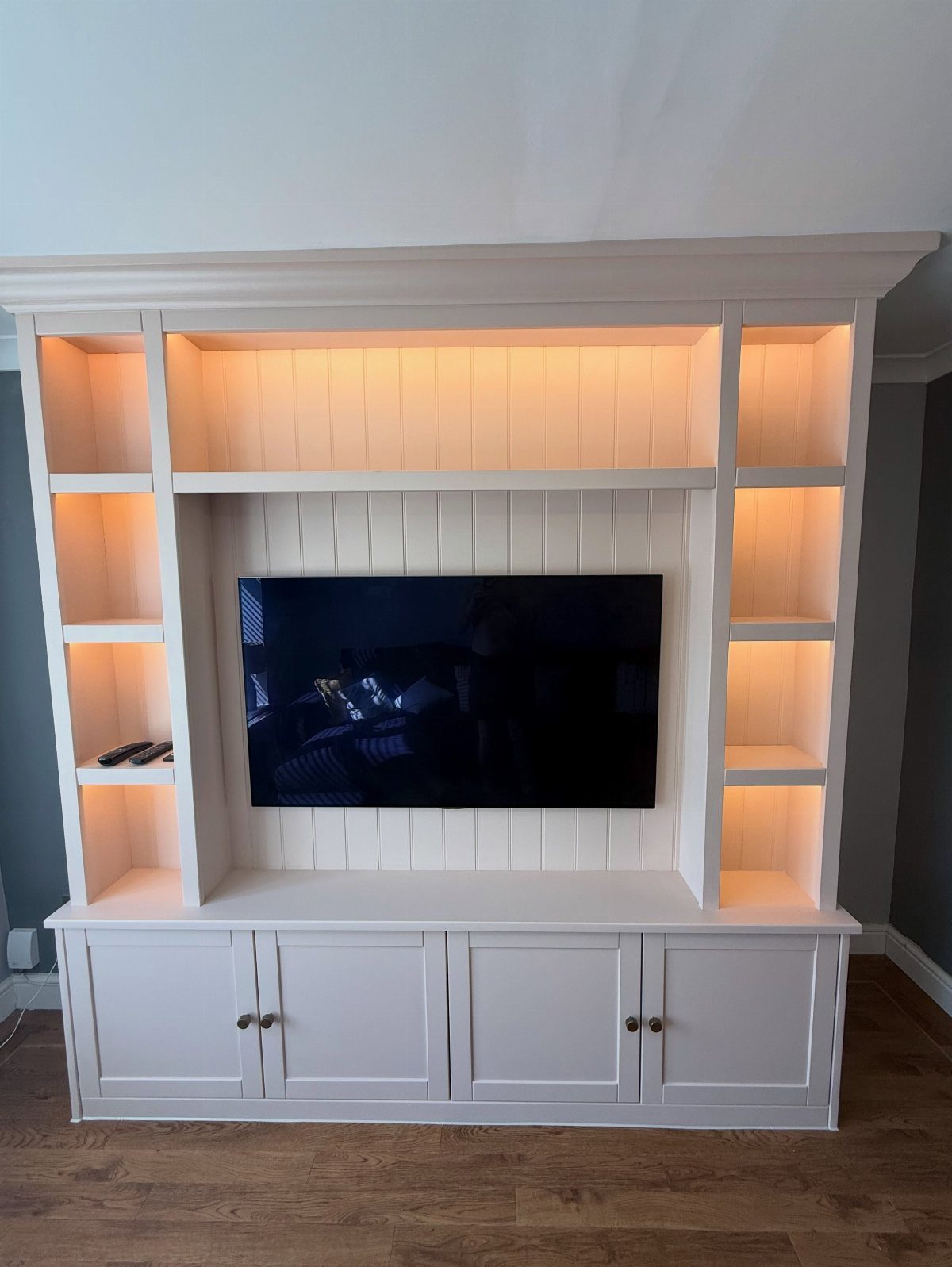 White entertainment center with integrated lighting, shelving, and cabinets surrounding a television.