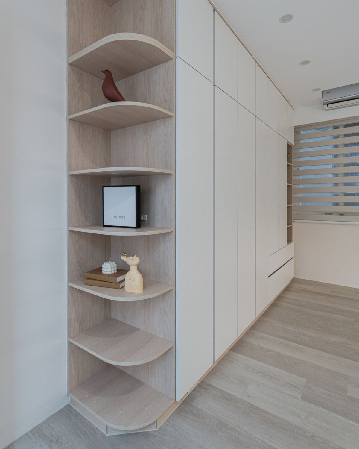 Curved light wood built-in corner shelves next to white seamless storage cabinets.