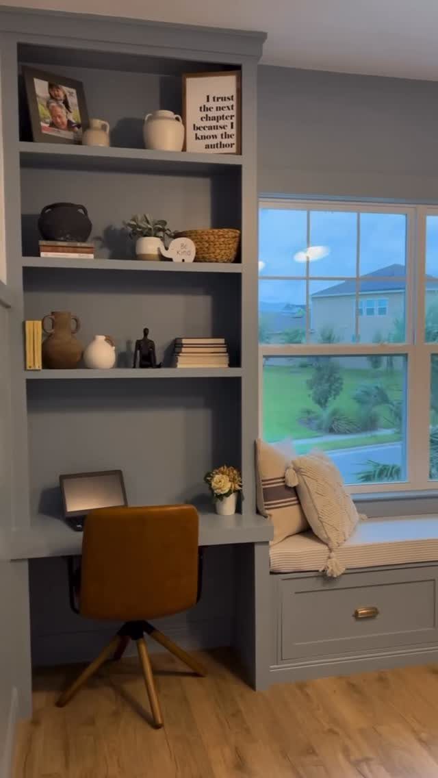 Grey built-in shelving unit with a desk and a cozy window seat nook.