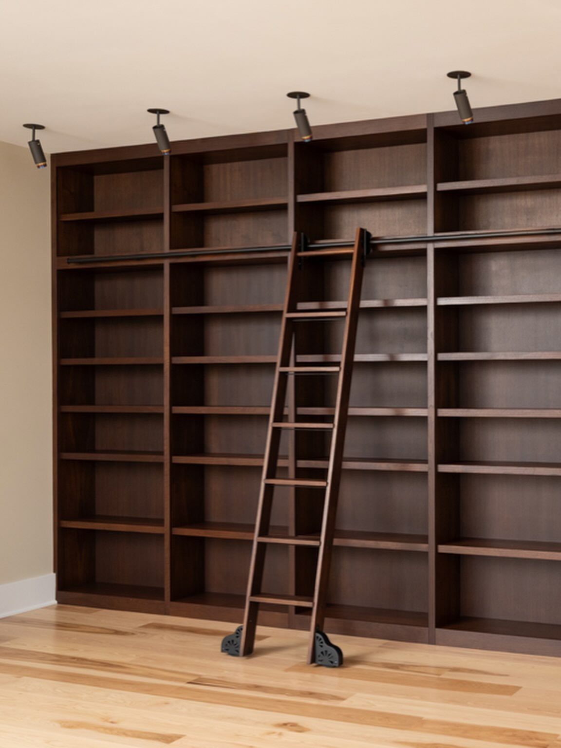 Dark brown floor-to-ceiling built-in bookshelves with a rolling wooden library ladder.