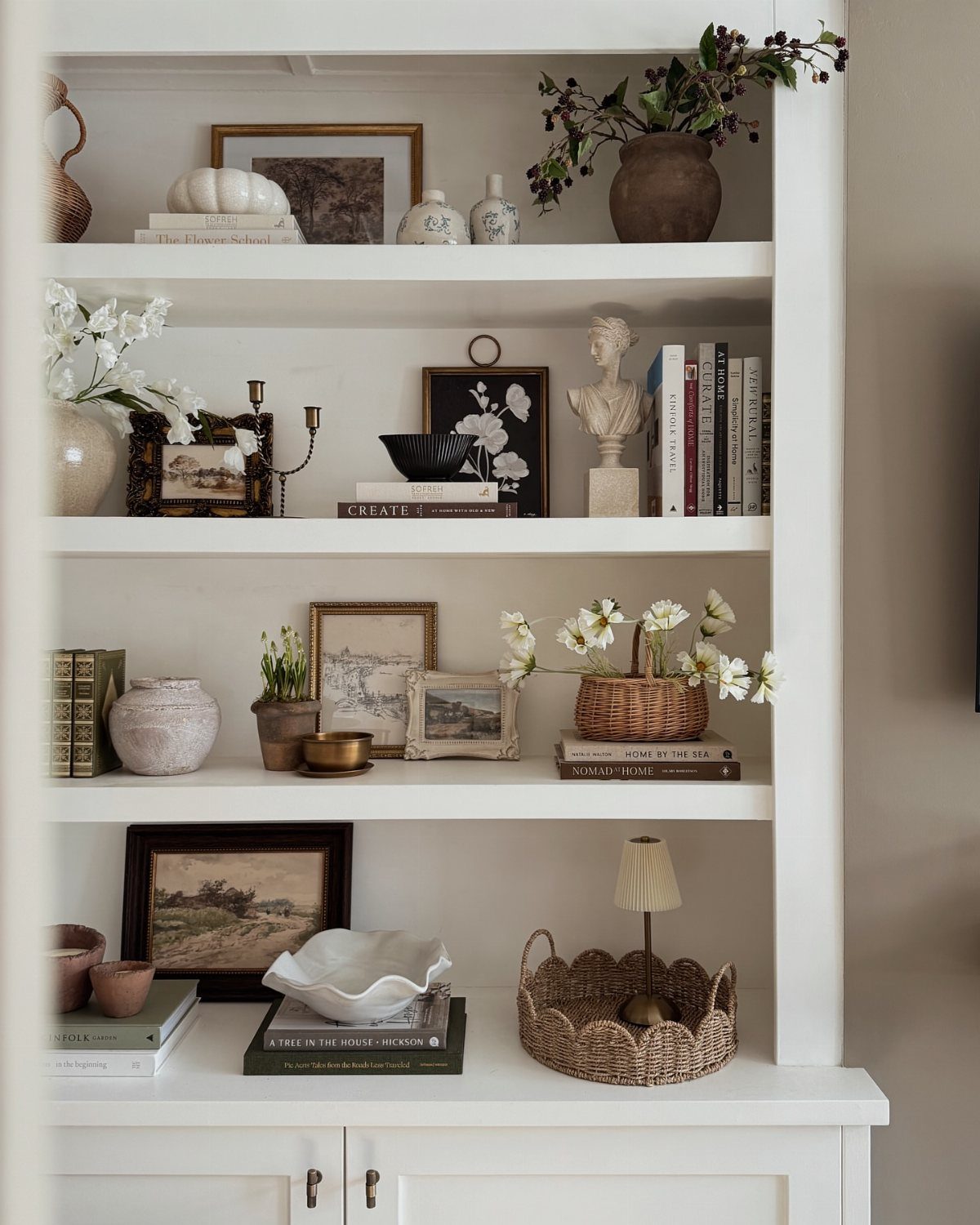 White built-in shelves styled with layered books, artwork, and decorative pottery objects.