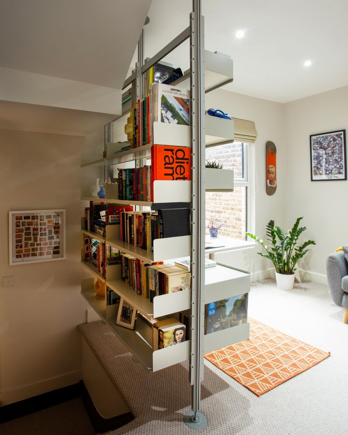 Grey metal modular shelving unit filled with books dividing a bright living room