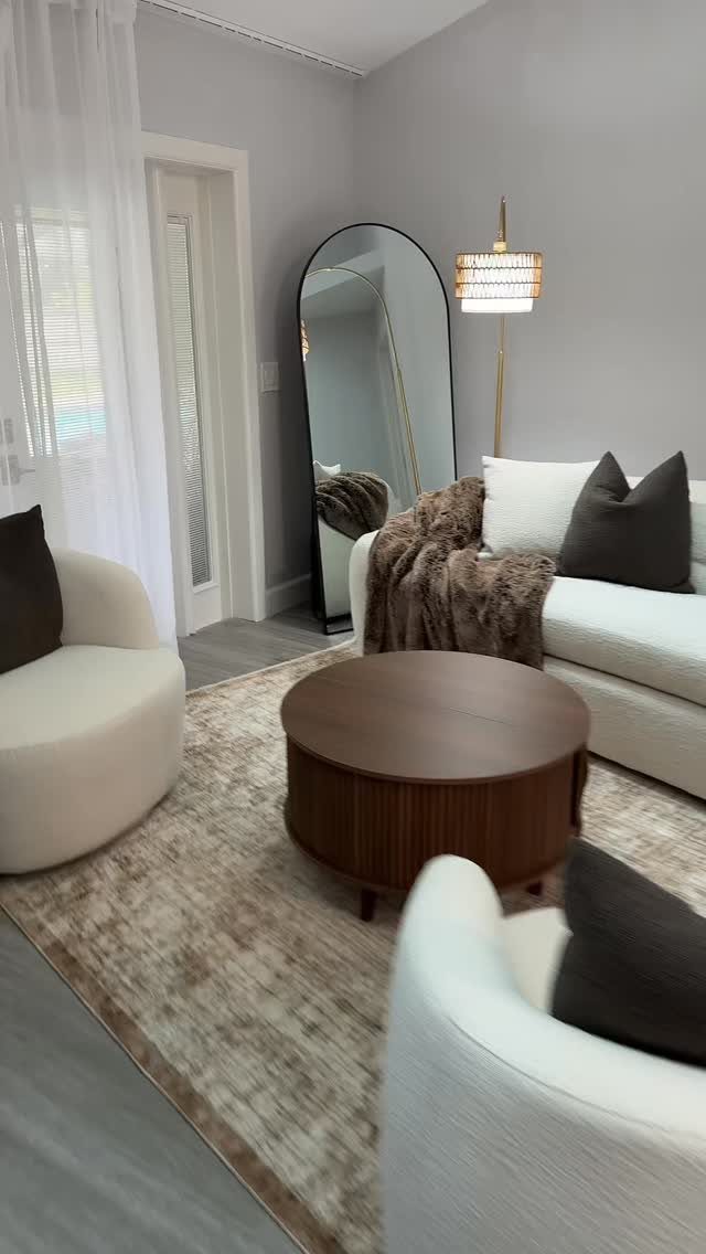 Round wooden coffee table surrounded by white curved armchairs and a cozy sofa.