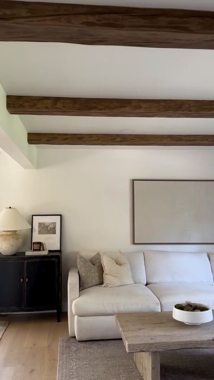 Dark wood ceiling beams over a white sofa and rustic wooden coffee table.