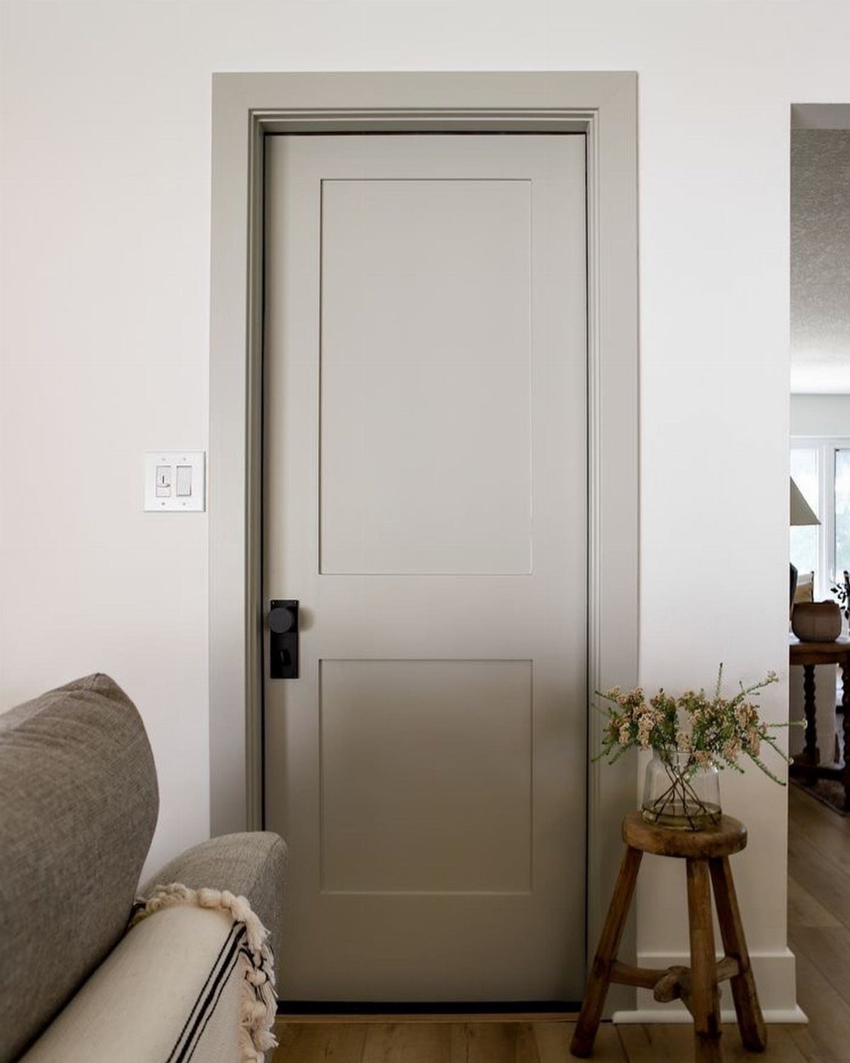 Grey painted interior door with black hardware and a small wooden flower stand.