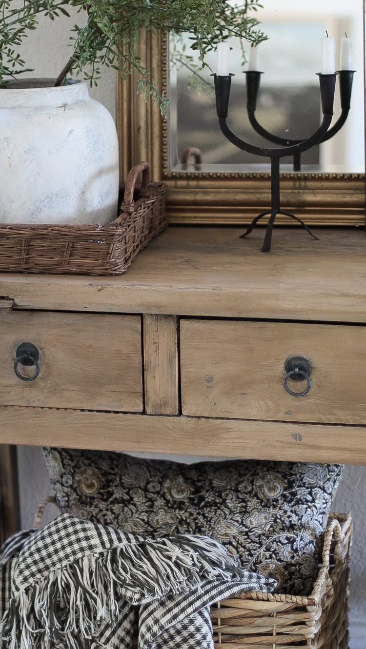 Wooden console table with a black candelabra, white pot, and woven baskets below.