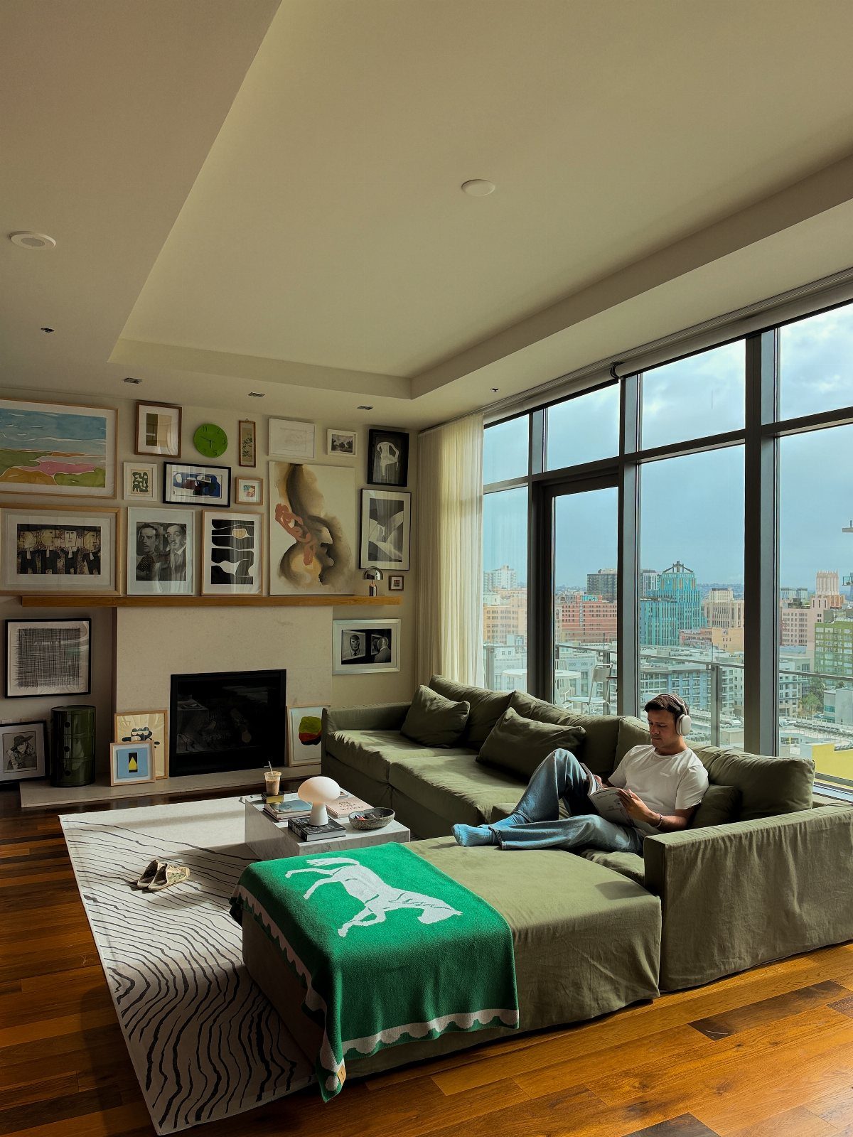 Modern living room with green sectional sofa, gallery wall, and city skyline view.