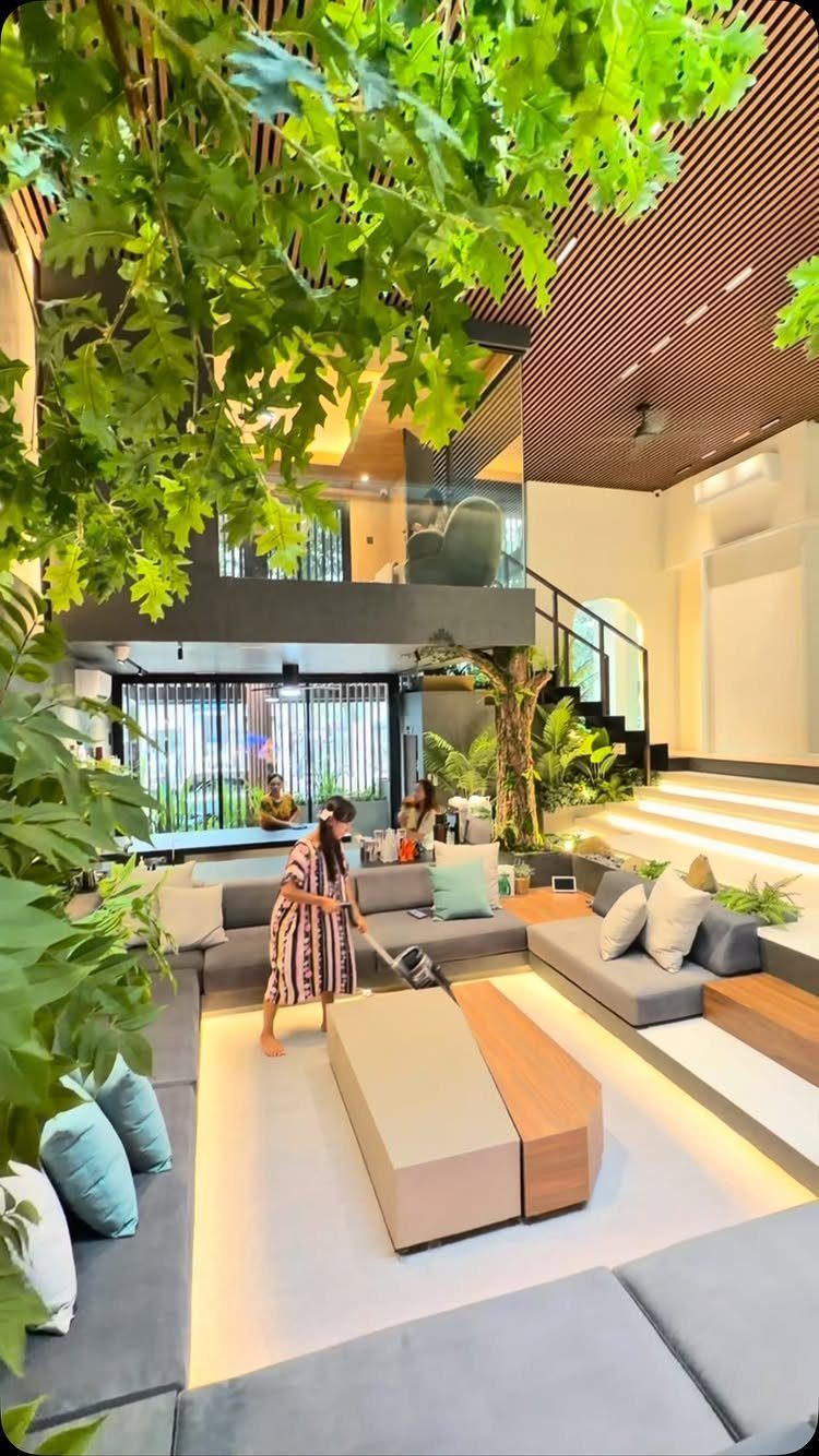 Modern living room with grey sectional sofa, wooden accents, and lush indoor greenery.