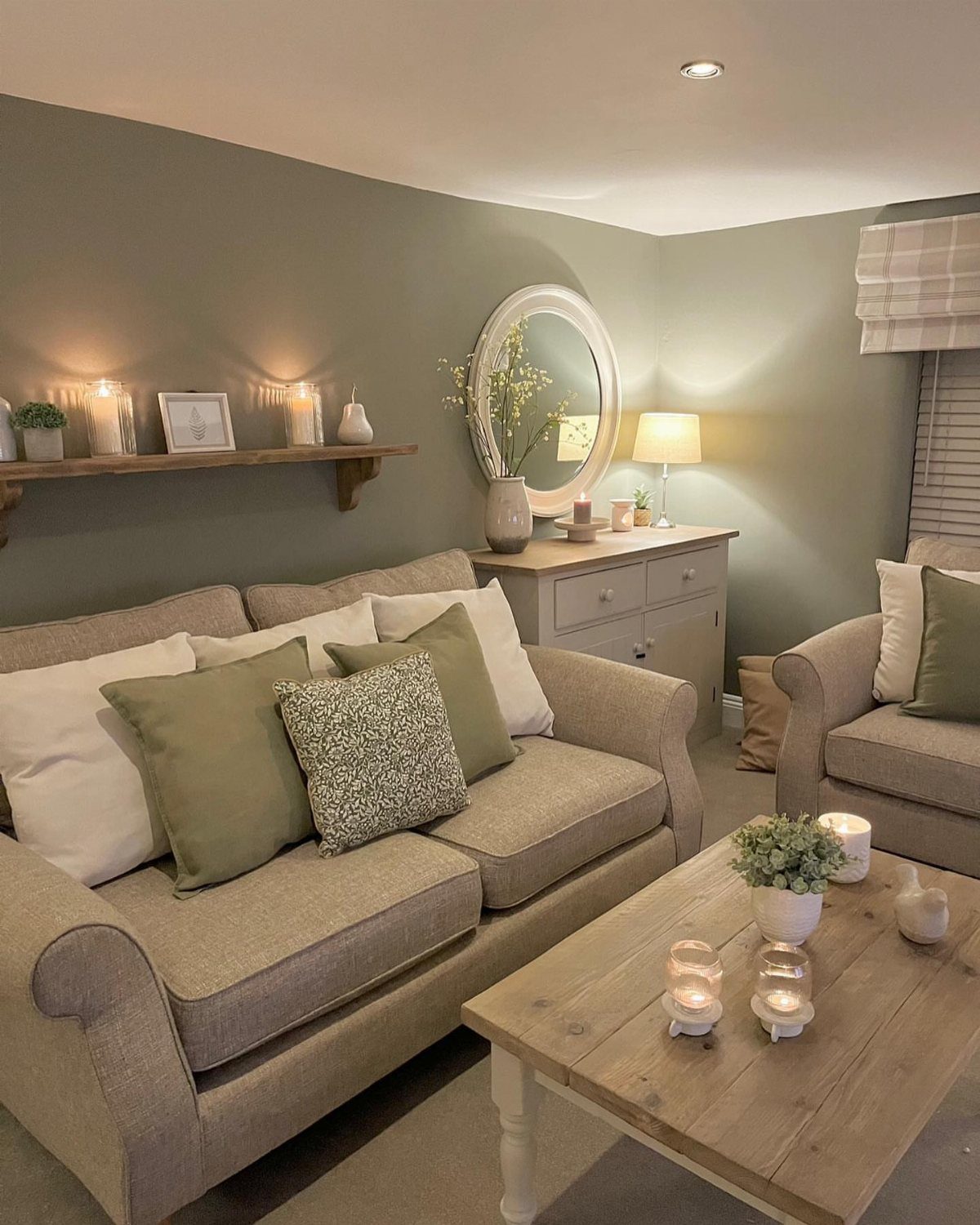 Beige sofa with green cushions in a room with sage green walls and plants.