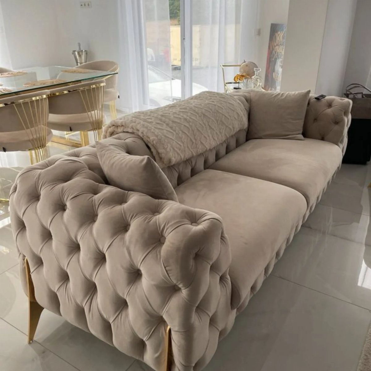 Beige tufted velvet sofa with gold legs and a fuzzy throw blanket.