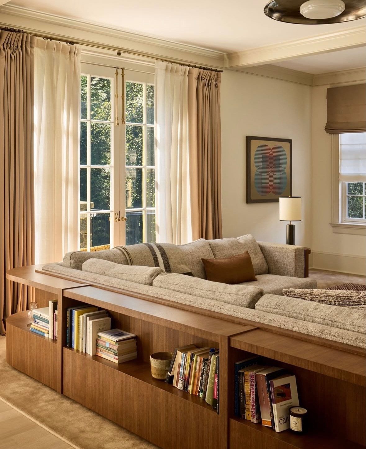 Beige sectional sofa with integrated wooden bookshelf placed in the middle of a room