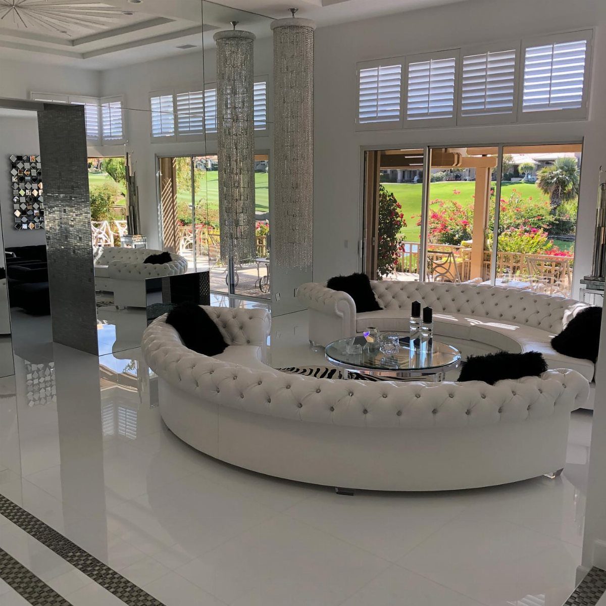 White tufted curved sofa with black cushions around a round glass coffee table.