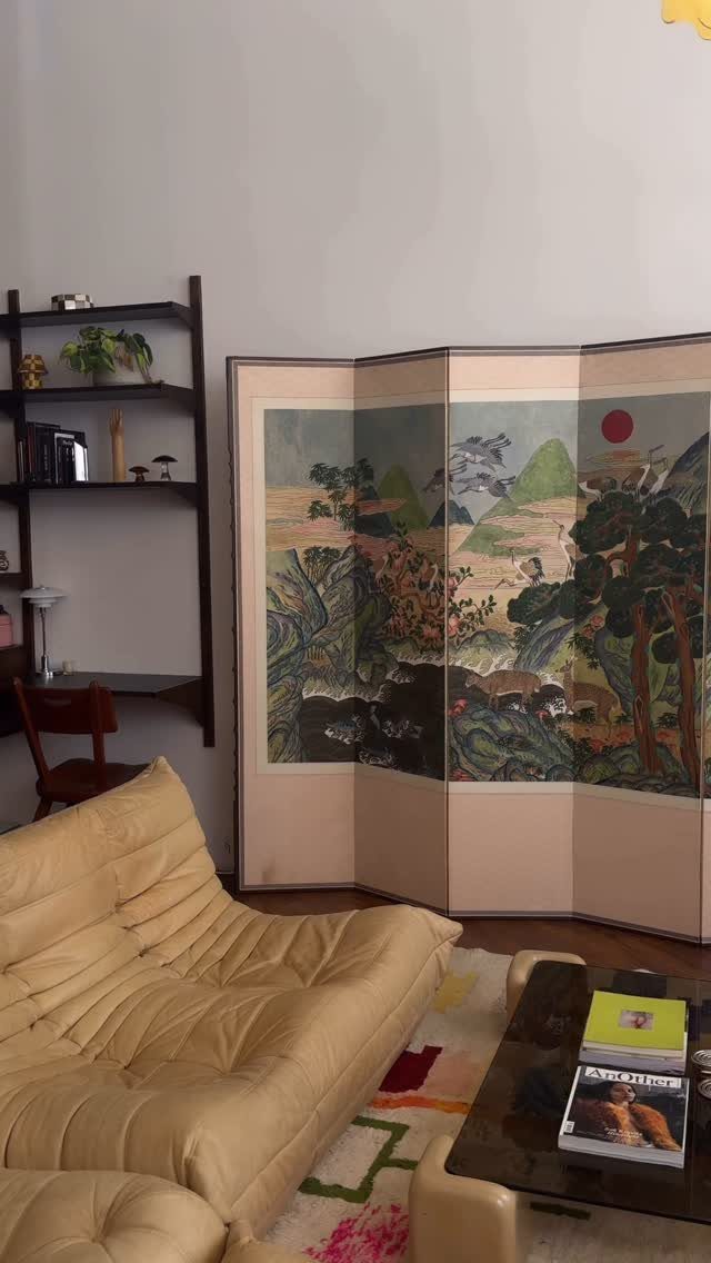 Beige tufted leather sofa with a folding landscape painting screen positioned behind it.