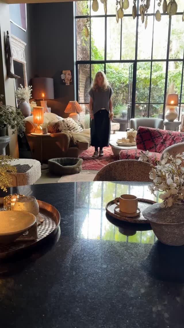 Woman standing in a living room with warm lamps illuminating a neutral couch.