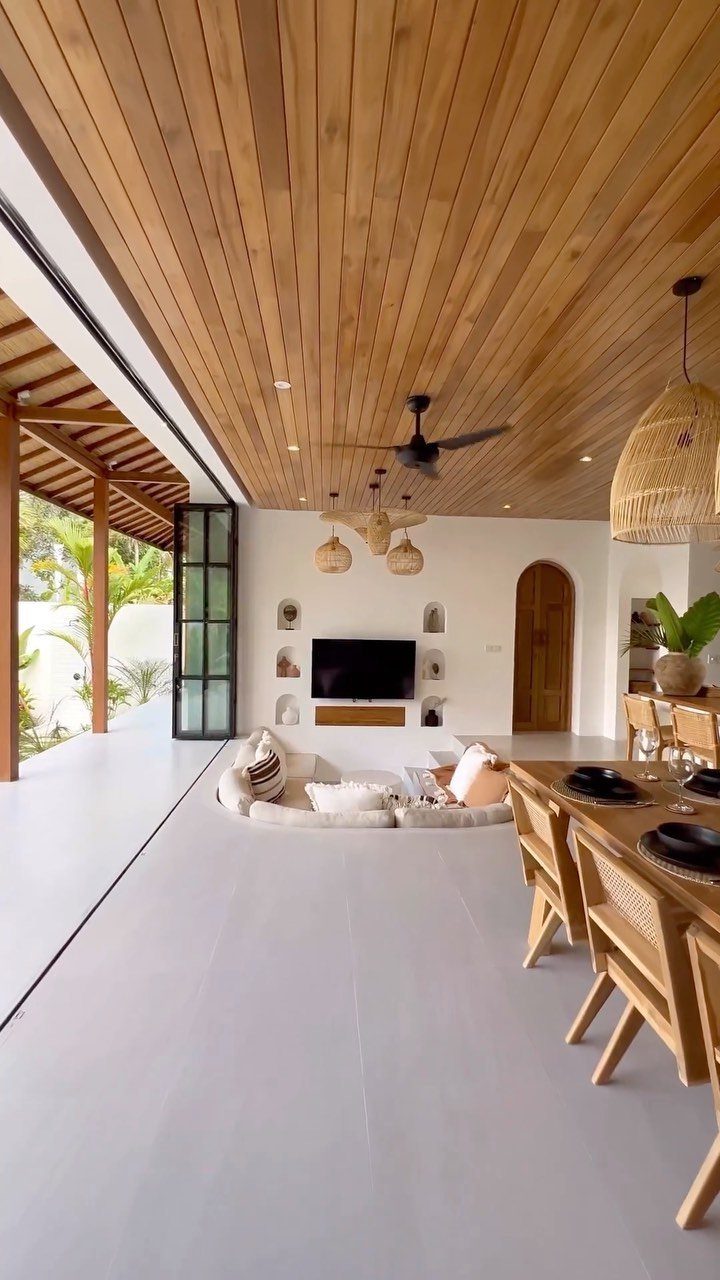 Modern rustic living room with wood ceiling, sunken seating, and wicker dining chairs.