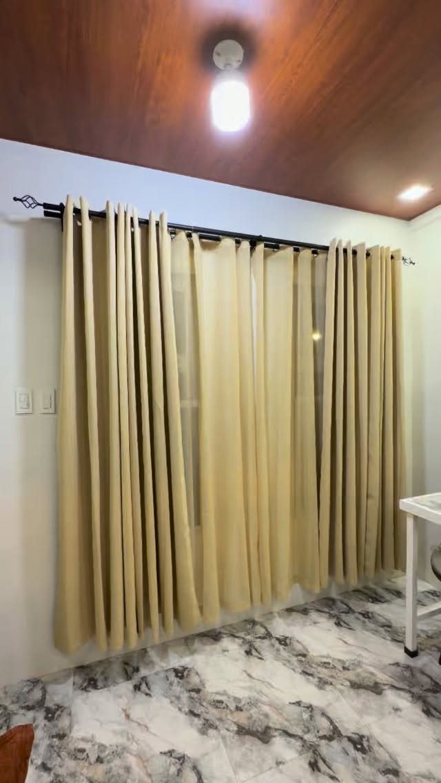 Beige curtains hanging from a black metal rod against a white wall.
