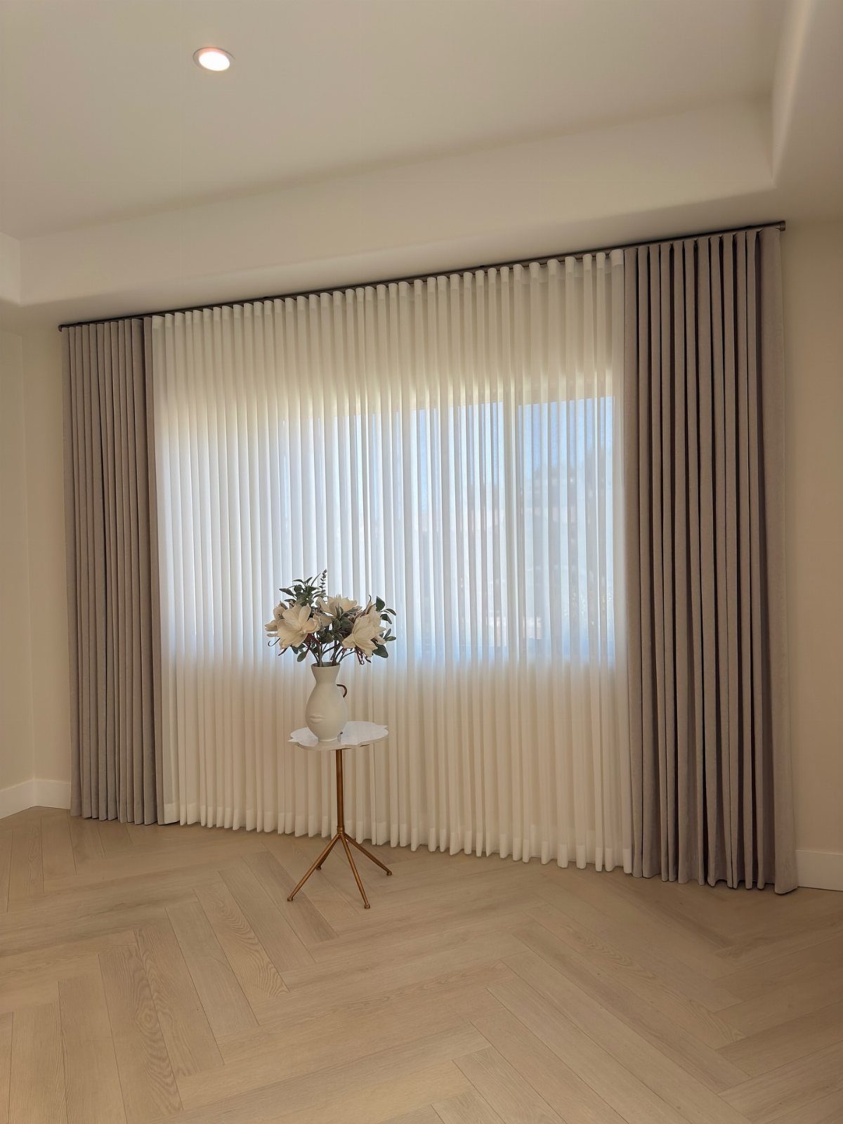 Custom grey and white draperies hanging in a living room with herringbone floors.