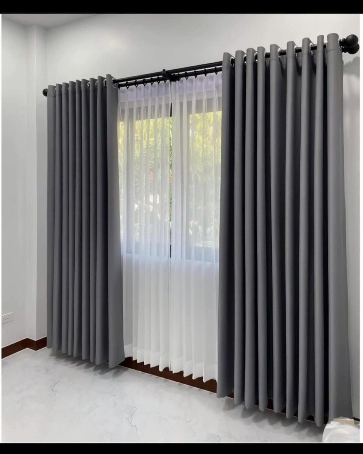 Grey grommet panels and white sheers hanging from a black curtain rod.