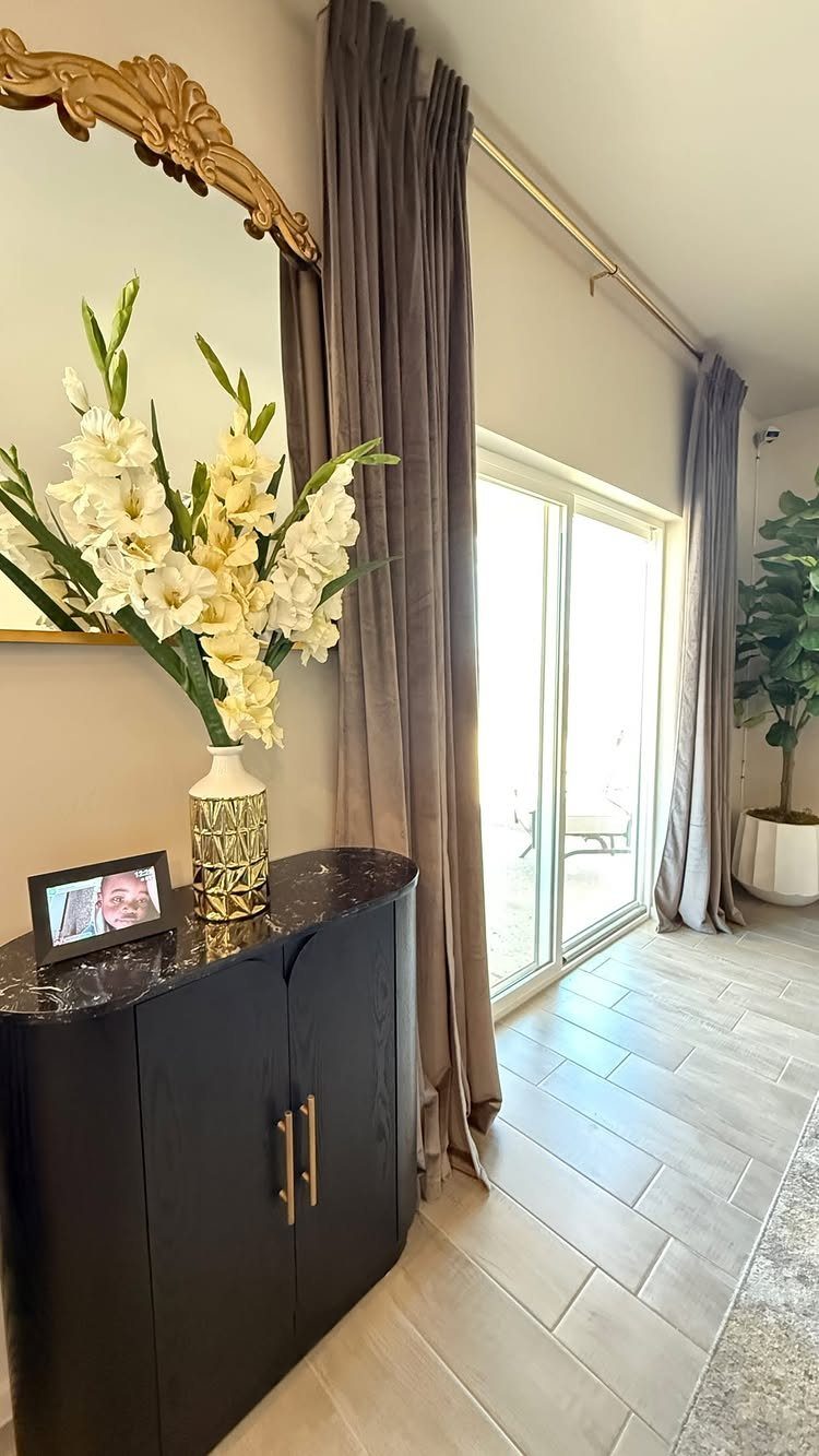 Grey curtains on a metal rod next to a black cabinet with white flowers.